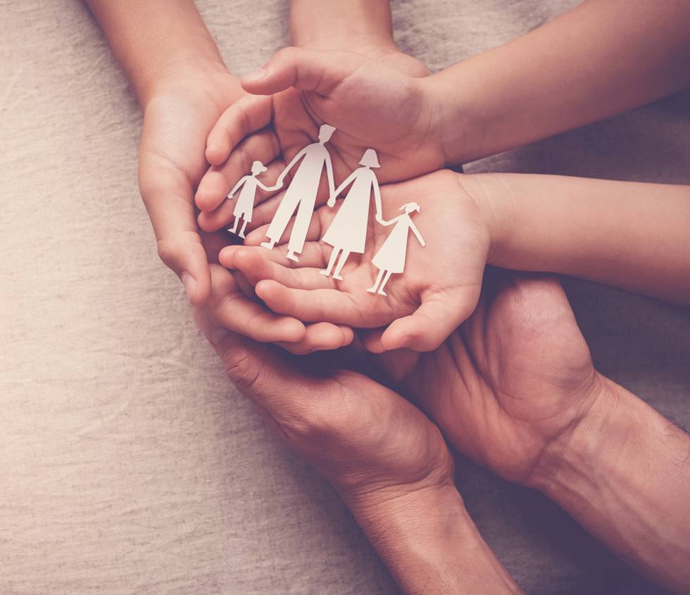 Paper cutout of a family inside a child's open palms, nested in its parents' hands